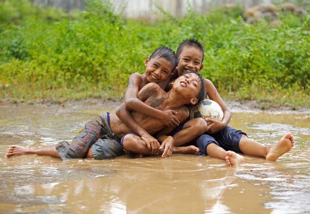 Three young boys playing in a mud after the rain , East Java , Indonesia